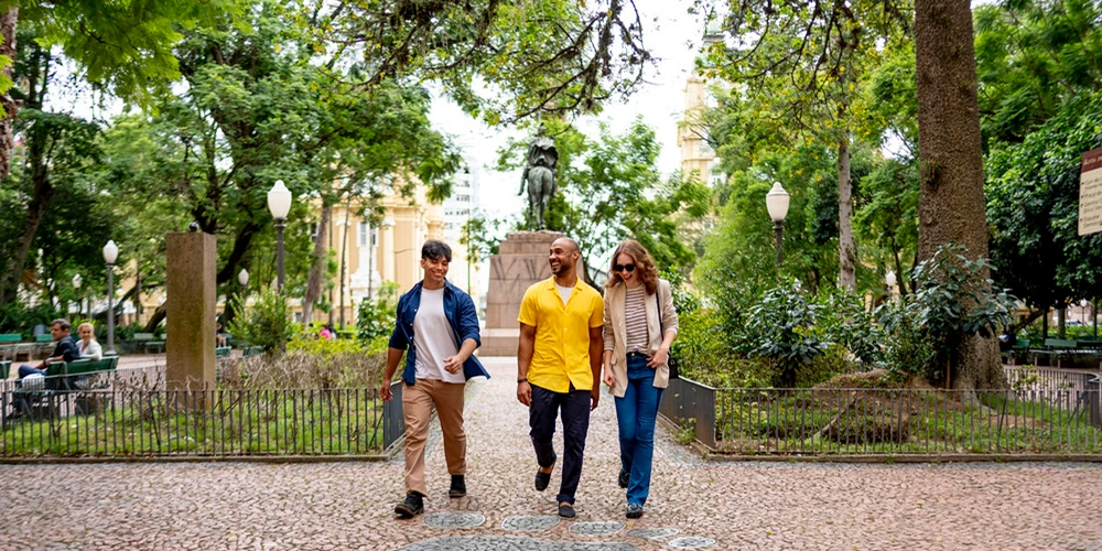Three travelers walking through a tree-lined historic square in Brazil