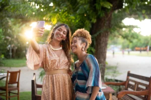 Two women smiling while taking a selfie in a leafy Brazilian park
